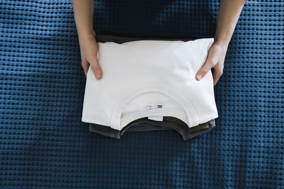 Manos doblando una remera blanca sobre una cama azul